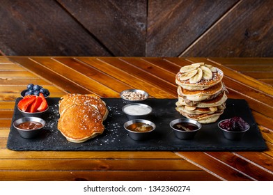 platter of pancakes with . double large stack of protein pancakes and array of different toppings on the side including strawberries blueberries maple syrup granola and sour cream 