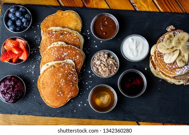 platter of pancakes with . double large stack of protein pancakes and array of different toppings on the side including strawberries blueberries maple syrup granola and sour cream 