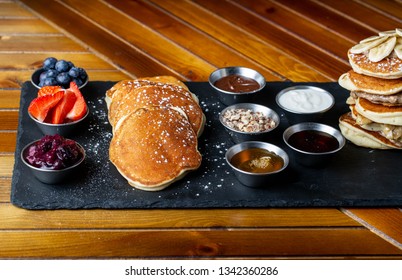 platter of pancakes with . double large stack of protein pancakes and array of different toppings on the side including strawberries blueberries maple syrup granola and sour cream 