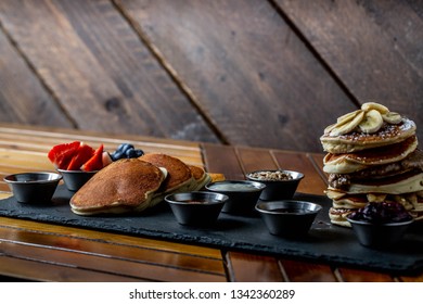 platter of pancakes with . double large stack of protein pancakes and array of different toppings on the side including strawberries blueberries maple syrup granola and sour cream 