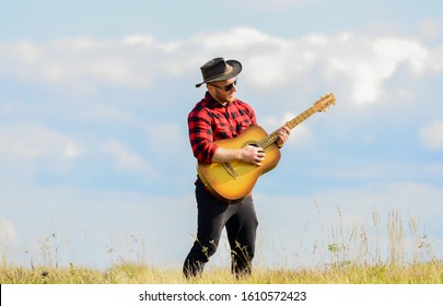 Play beautiful melody. Country music concept. Guitarist country singer stand in field sky background. Inspired country musician. Hiking song. Handsome man with guitar. Country style. Summer vacation.