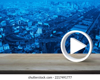 Play Button 3d Icon On Wooden Table Over Modern City Tower, Street, Expressway And Skyscraper, Business Music Online Concept