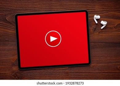 Play button on the screen of tablet and wireless earphones on dark wooden surface