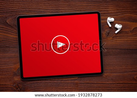 Play button on the screen of tablet and wireless earphones on dark wooden surface