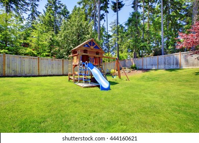 Play Kids Ground Area With Chute In Fenced Backyard. House Exterior.