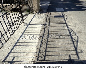 Play Of Light And Shade: Reflection Of An Ornate Cast Iron Fence On Asphalt. Taken On A Sunny Cloudless Afternoon. No People. Taken In Nassau, The Bahamas, One Of The Backstreets.