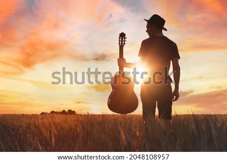 play music, silhouette of musician with guitar at sunset field outside