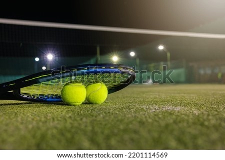 play tennis in dark with artificial lighting. racket and balls on outdoor court with copy space