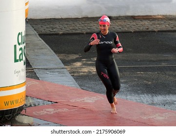 PLAYA BLANCA, LANZAROTE, SPAIN - MARCH 9, 2022: Female Triathlon Competitor In Wet Suit Leaving Swimming Stage.