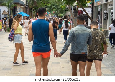 Playa del Carmen, Quintana Roo, Mexico - February 06.2022 Gay couple walking down a busy street  holding hands. Two boys in love walking together, view from the back.