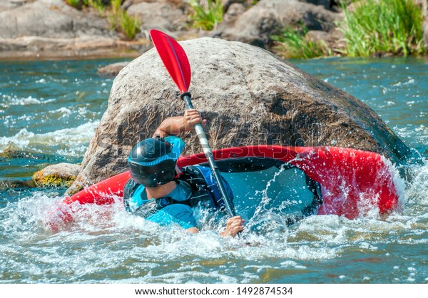 Playboating. A man sitting in a kayak with oars in\
his hands performs exercises on the water. Kayaking freestyle on\
whitewater. Eskimo\
roll.