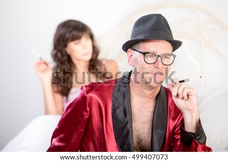 Playboy in hat with pretty woman in the background on white bed
