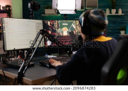 Player doing online live streaming with video games. Woman using gameplay on computer to stream and looking at monitor with chat. Person broadcasting and playing games with microphone.