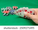 player Hand holding royal flush in hearts with poker chips on green felt background