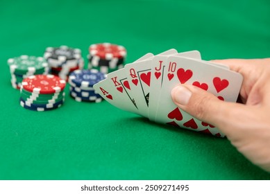 player Hand holding royal flush in hearts with poker chips on green felt background