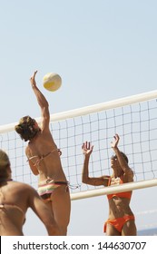 Player Jumping To Spike Volleyball Over Net As Opponent Defends On Beach