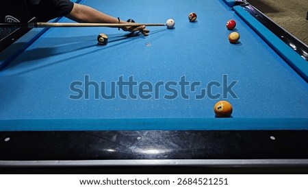 A player lines up a precise pool shot on a blue billiards table, with several balls positioned for play. Calm, competitive atmosphere, indoor recreation, careful aim and skill.