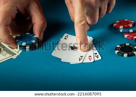 The player points with his finger at a winning three kind or set combination in poker game on a blue table with chips and money in club.