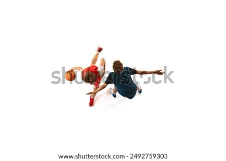 Player in red dribbling, while opponent in blue attempts to block him from ground against white studio background. Aerial view. Concept of professional sport, competition, match, team games. Ad