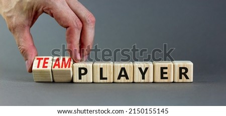 Player or teamplayer symbol. Businessman turns wooden cubes and changes concept words Player to Teamplayer. Beautiful grey table grey background, copy space. Business player or teamplayer concept.