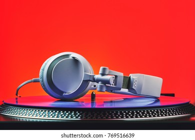 Player turntable vinyl records and white headphones in red light. Equipment for the disc jockey. Sound technology for DJ to mix and play music. Violet vinyl plate. Vinyl turntable in red light