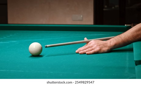 The player's hand with the cue hits the white cue ball on a green table. Playing russian billiard game. Accurate shot. Close-up of impact.