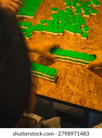 Players' hands stacking and pushing rows of green-backed Mahjong tiles face down to build walls on a wooden particle board table.