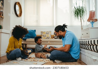 A playful african american family is spending quality time together at home and playing games with a wooden toy while sitting on the floor in a living room. An african american family having playtime. - Powered by Shutterstock