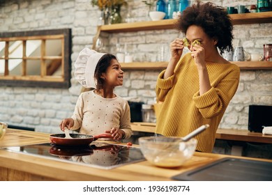 Playful African American mother and daughter having fun with vegetables while preparing food in the kitchen. - Shutterstock ID 1936198774