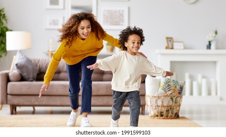 Playful African American Mother Trying To Catch Excited Small Child Son While Playing Together At Home, Playful Mom And Kid Running And Having Fun In Living Room. Happy Family Enjoying Leisure Time