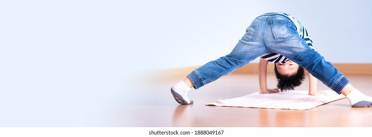 A Playful Asian Happy And Healthy Little Boy (3-6 Years) Bend Over His Body Headstand And Looking Between His Legs In The Kindergarten Montessori Classroom. Child Development, Kids Stretching. Banner.