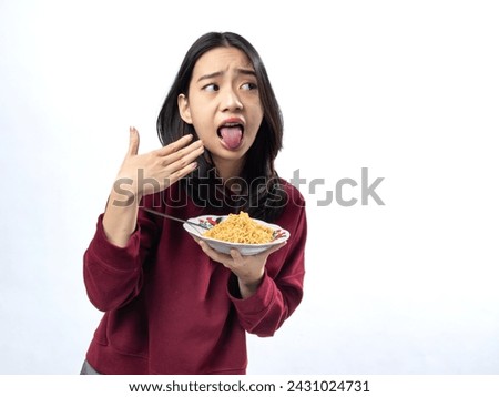 Playful Asian woman gesturing too hot while tasting spicy noodles, in a burgundy top, white backdrop