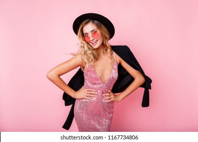 Playful Blond Girl With Trendy Round Glasses Dancing And Having Fun  On Pink Background.  Party Dress, Black Hat. 