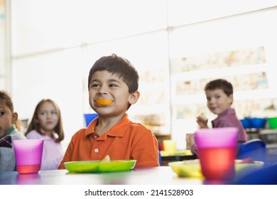 Playful boy holding orange slice in mouth at school at snack time