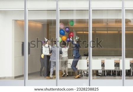 Playful business people in party hats celebrating balloons in conference room