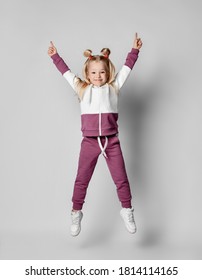 Playful cheerful girl in a stylish modern pink gray sports sweatshirt with a hood and trousers is jumping high on a gray background. Smiling child when jumping widely spreads his legs and arms.