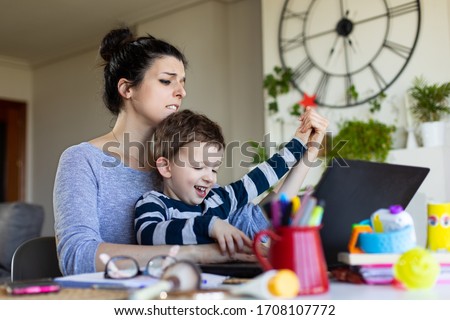 Playful child annoying his mother while she tries to tele work. Telecommuting issues and family conciliation concept.