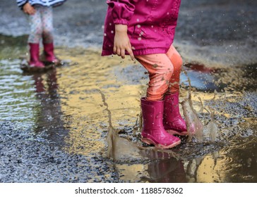 Playful child outdoor jump into puddle in boot after rain