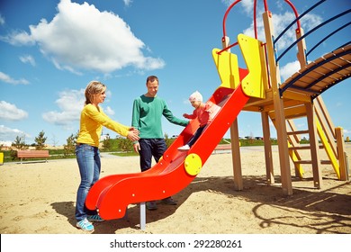 Playful Child With Parents At The Playground Outdoor. Mom, Dad And Child