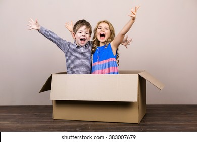 Playful childhood. Little children having fun with cardboard box. Children cheerfully smiling