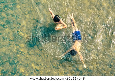 Playful children swimming in Nam Song river in Vang Vieng - Real everyday healthy life and fun of kids in Laos PDR countryside region - Neutral nostalgic color tone with main focus on boy out of water