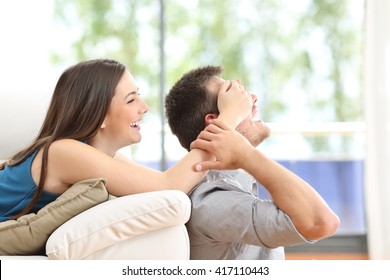 Playful couple covering eyes at home with a window in the background - Powered by Shutterstock