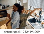 Playful couple dancing and singing while washing dishes together at home. 