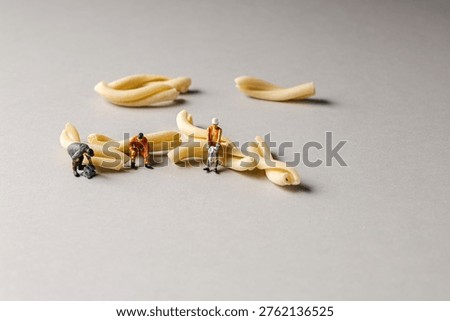 a playful and creative conceptual image featuring tiny miniature people figures working on uncooked pasta