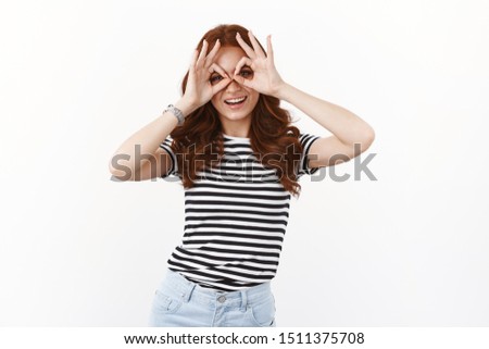 Playful cute young redhead girl in striped t-shirt looking through circles, making finger-glasses and smiling joyfully, tilt head, fool around, do goofy grin as having fun, enjoy summertime holidays