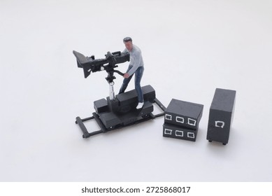 playful diorama of tiny figures making a movie: a cameraman on a dolly, a