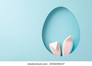 Playful Easter inspiration photo. Top view of humorous bunny ears peeking from an ovoid gap on a tranquil blue setting, with space for your text Stock-foto