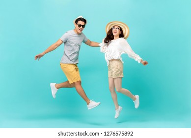 Playful Energetic Asian Couple In Summer Beach Casual Clothes Jumping Isolated On Light Blue Background Studio Shot