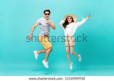 Playful energetic Asian couple in summer beach casual clothes jumping isolated on light blue background studio shot
