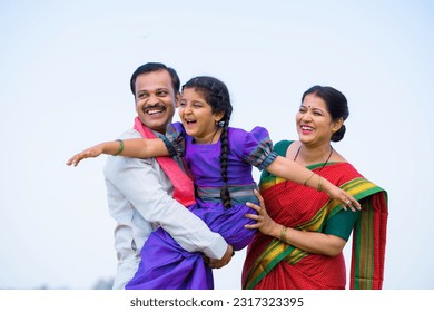 Playful excited indian girl kid while holding by father with mother near farmland - concept of parents support, family bonding and happiness
